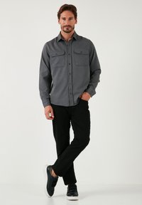 Grijze langmouw shirt met twee borstzakken, knopen aan de voorkant en een relaxte pasvorm, gecombineerd met zwarte broek en zwarte sneakers.