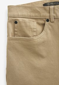 Pantalon beige coupe droite en tissu texturé, avec une poche avant, des passants de ceinture et un détail de bouton noir sur la poche.