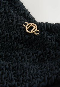 Țesătură neagră texturată, cu detalii plisate și un accent de hardware circular auriu. Designul este complex și cu multiple dimensiuni.