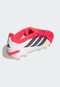 Κόκκινο και λευκό ποδοσφαιρικό παπούτσι Adidas Predator με μαύρες ρίγες και διαφανείς τάπες, απομονωμένο σε λευκό φόντο.