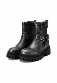 Botas de tobillo de cuero negro con una suela de goma texturizada y chunky, cierre lateral con cremallera y correas decorativas con hebillas de metal y adornos.