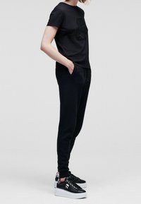 Svart t-shirt med kort ärm och en texturerad svart grafik på framsidan, kombinerad med svarta avsmalnande joggers och plattformssneakers.