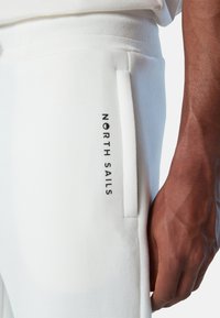 Pantalones de chándal blancos hechos de tela suave, con cintura elástica y un bolsillo lateral con "NORTH SAILS" impreso en negro.