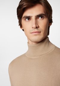 Beżowy sweter z golfem o dopasowanym kroju i żebrowanej strukturze, z wysokim kołnierzem i gładkim materiałem.