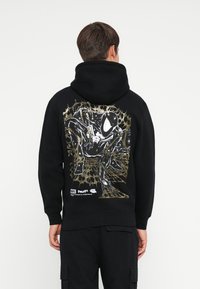 Black hoodie featuring a graphic print on the back with a character in white and gold outline against a spider web design.