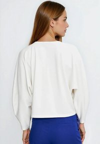 Biały, długorękawowy top o luźnym kroju, z okrągłym dekoltem i rozszerzanymi rękawami, zestawiony z niebieskimi spodniami. Gładka tkanina o gładkiej fakturze.