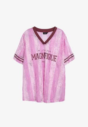 Roosa pits T-särk V-kujuga ja lühikeste varrukatega. Omab vertikaalseid triibusid ja pruunisid aktsente, mille keskel on tekst "MAGNIFIQUE".