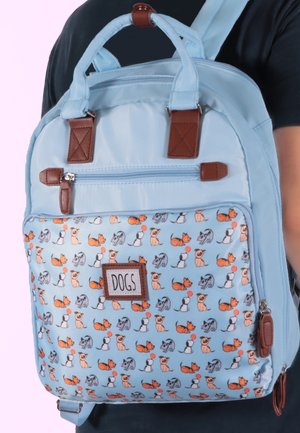 Helle blaue Rucksack mit braunen Lederakzenten und einer Fronttasche mit einem verspielten Hundemuster in verschiedenen Farben. Eingearbeitete Reißverschlussfächer.