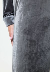 Grauer Velvet-Stoff, der eine weiche, glatte Textur mit einem subtilen Glanz zeigt. Enthält ein Manschettendetail an einem Ärmel sowie eine Nahaufnahme.