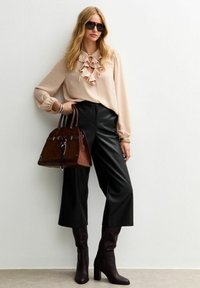 Blusa beige con escote con volantes, pantalones de pierna ancha de imitación cuero negra, bolso marrón con detalles en plata y botas marrones hasta la rodilla.