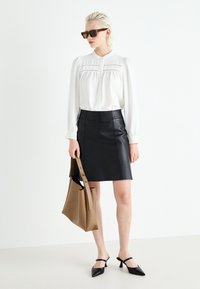 Bílá halenka s dlouhým rukávem a sklady, černá kožená mini sukně a černé slingback muly. Na jednom rameni visí béžová kabelka.