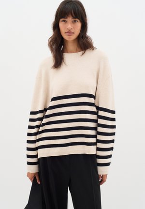 Maglione crema con strisce orizzontali nere, caratterizzato da una vestibilità comoda, scollo a girocollo largo e polsini a costine. Tessuto a maglia testurizzato.