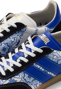 Paire de baskets bleu, blanc et noir avec des lacets blancs, des panneaux en tissu à motifs et "CAVAL" imprimé en or sur la languette.