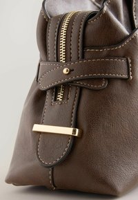 Close-up van de hoek van een bruine leren handtas met een gouden rits, sluiting en gedetailleerde stiksels op het gladde, textuur oppervlak.
