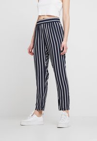 Marinblå randiga byxor med vita vertikala ränder, elastisk midja, smalnande ben och ett lätt material, i kombination med vita sneakers.