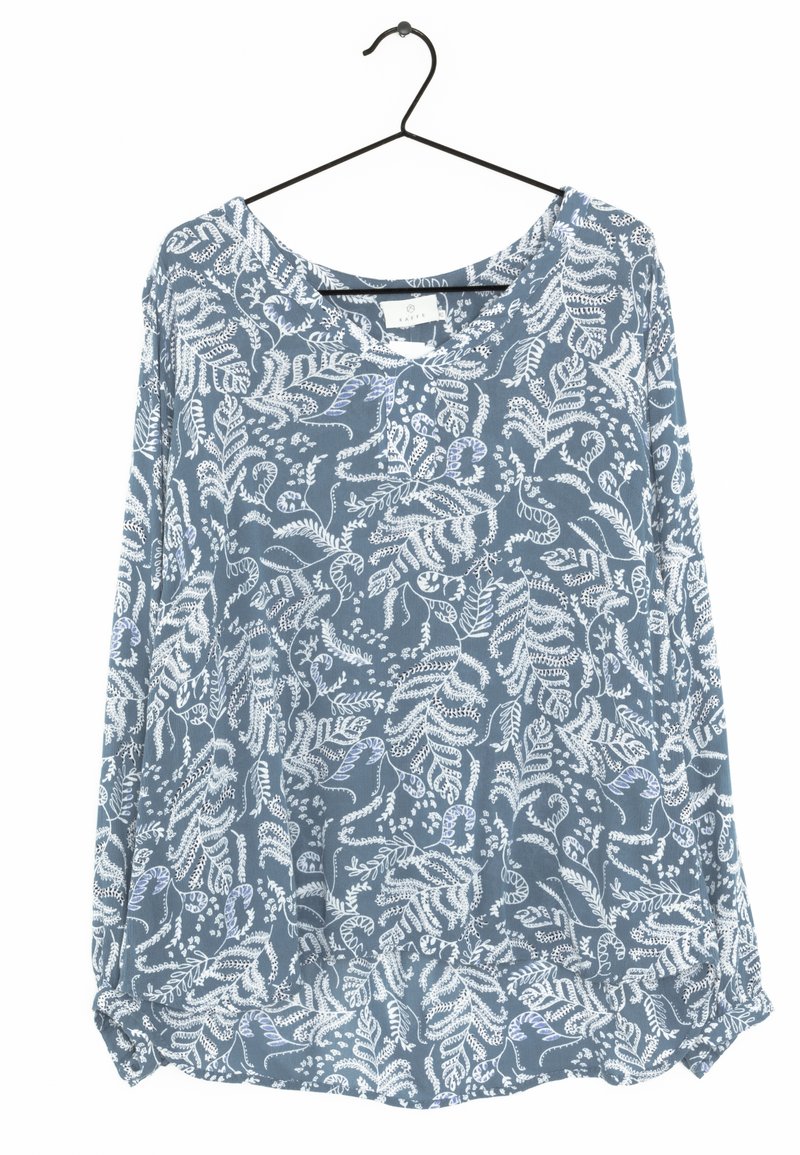 Chemise bleue à manches longues avec motifs floraux et feuillages blancs suspendue sur un cintre en fil noir.