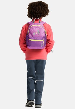 Bambino con capelli ricci che indossa una giacca color corallo e pantaloni scuri, con uno zaino viola con illustrazioni di animali sulla schiena.