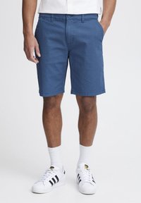 Blå shorts med et strukturert mønster, med knappeforbindelse, sidelommer og rett snitt. Kombinert med hvite joggesko og sokker.