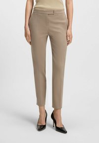 Beige op maat gemaakte broeken met een slim fit, voorzien van voornaad, zijzakken en een gladde textuur, gecombineerd met zwarte puntige hakken.