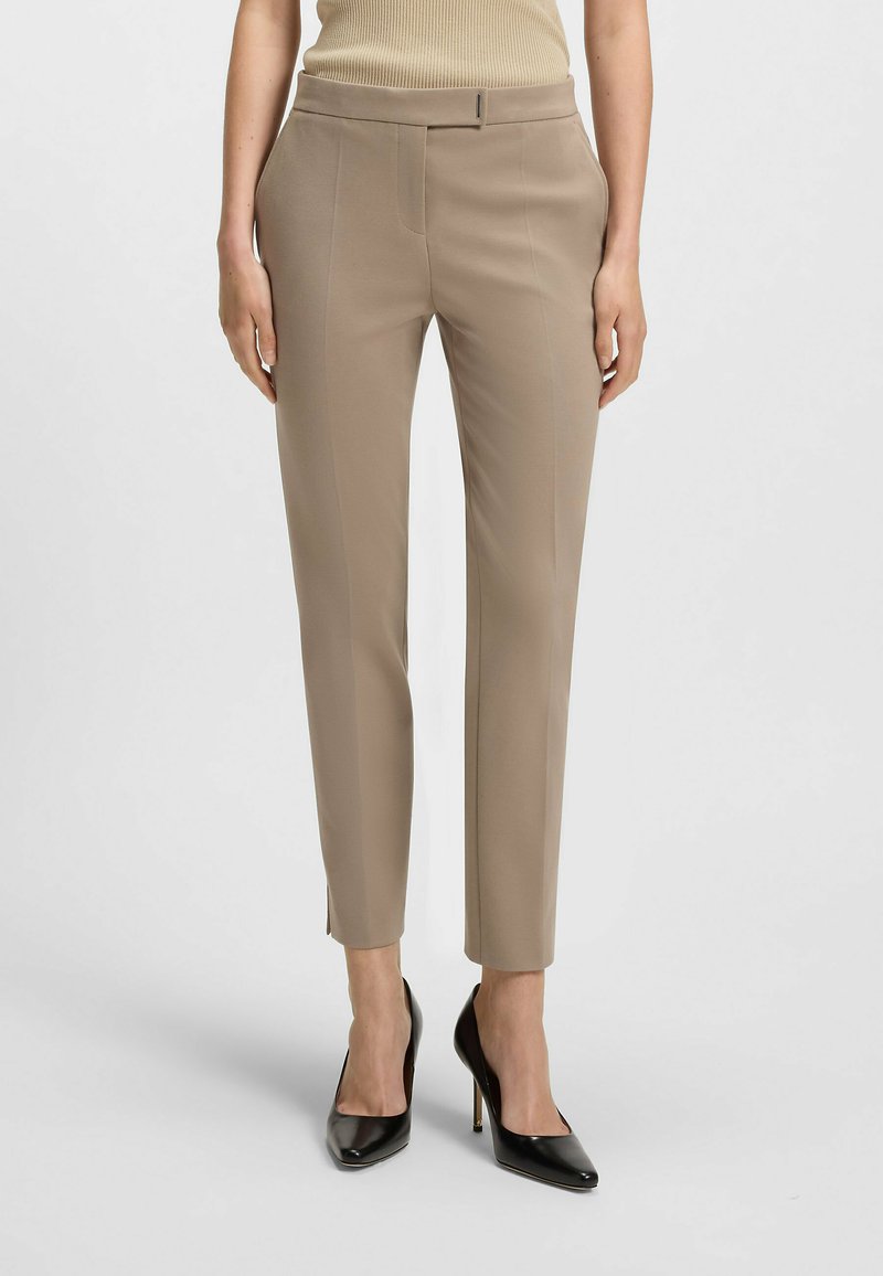 Beige op maat gemaakte broeken met een slim fit, voorzien van voornaad, zijzakken en een gladde textuur, gecombineerd met zwarte puntige hakken.