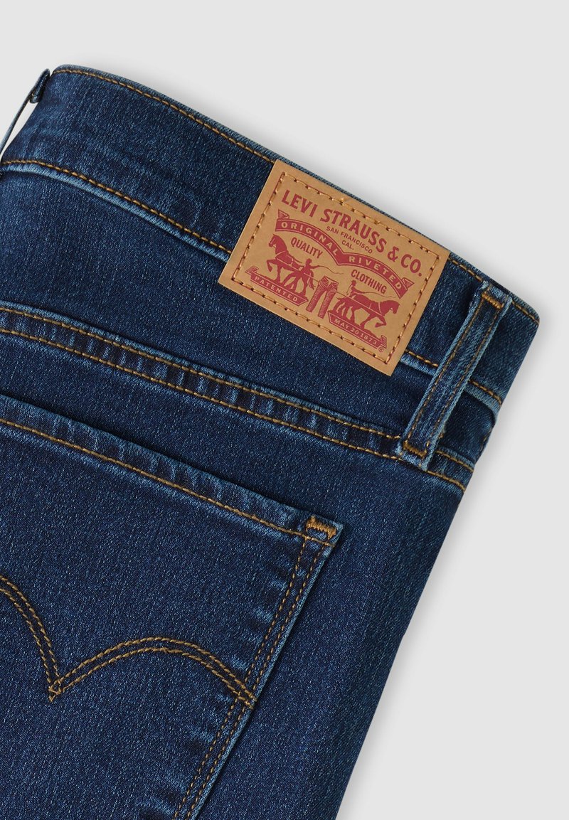 Jean en denim bleu foncé montrant une poche arrière et une étiquette en cuir marron Levi Strauss & Co. avec le logo de la marque et des détails de couture.