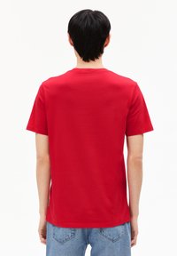 T-shirt rouge à manches courtes en coton lisse. Col rond et ourlet droit. Porté avec un jean en denim bleu clair, montré de dos.