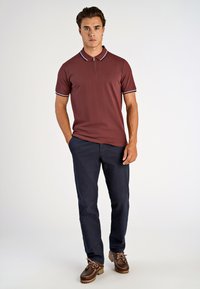 Bordowy polo z zapięciem pod szyją, białymi paskami akcentowymi i haftowanym logo, w połączeniu z granatowymi chinosami oraz brązowymi butami sznurowanymi.