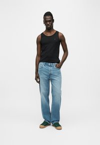 Μαύρο αμάνικο τοπ, ανοιχτό μπλε τζιν με ίσια γραμμή και πράσινα αθλητικά παπούτσια με ταμπά σόλα. Ομαλή υφή, casual σχέδιο, με ελάχιστο λογότυπο στο τοπ.