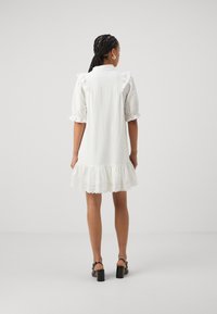 Vitt linne kort klänning med puffärmar och spetsdetaljer vid fållen. Har textilstruktur och en utsvängd silhuett.