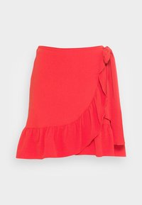 Jupe rouge avec un ourlet froncé et un nœud sur le côté. Fabriquée en tissu léger, elle présente une texture douce et un design fluide.