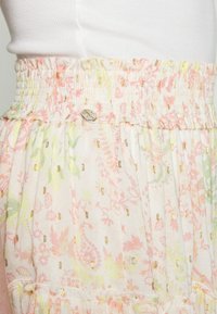 Sainha com padrão floral em tons de rosa pastel e verde, apresentando uma cintura franzida e detalhes em dourado em todo o tecido.