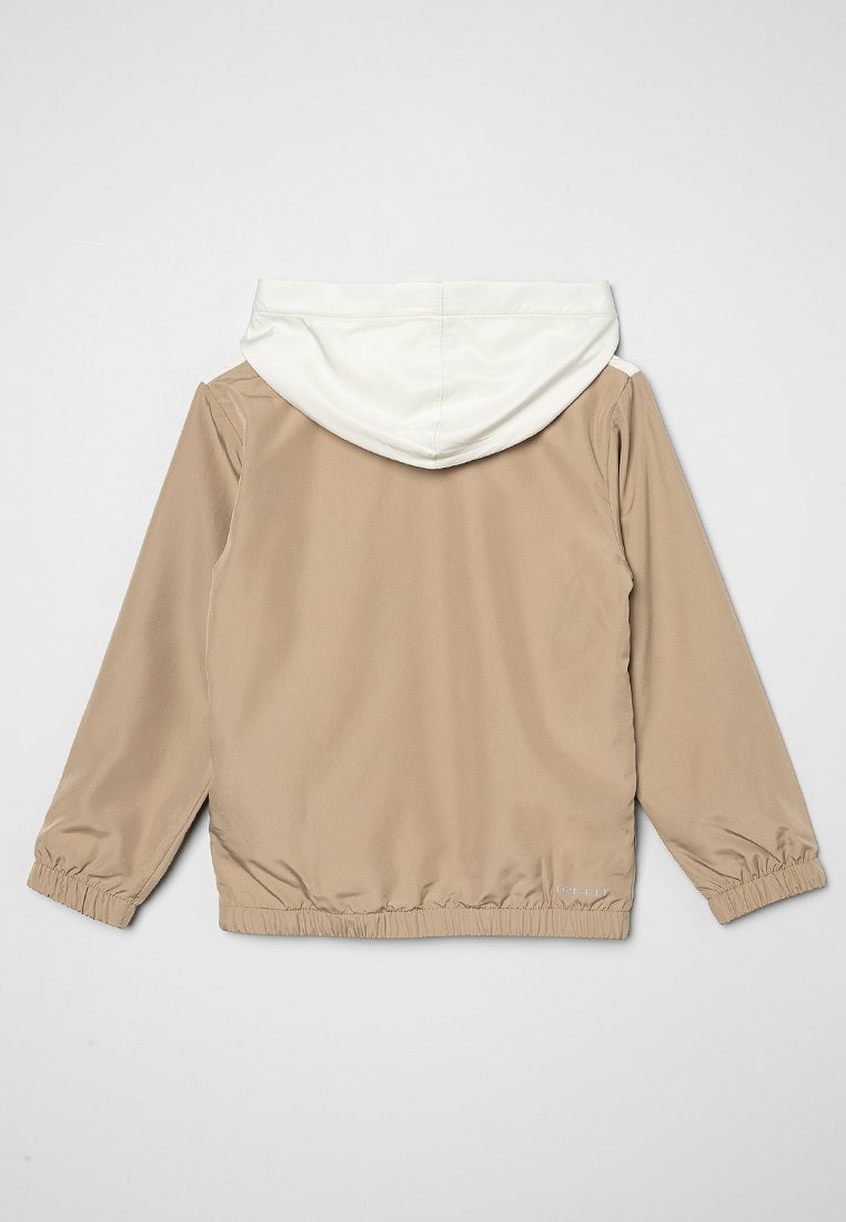 Veste coupe-vent beige avec une capuche blanche, des poignets et une taille élastiques, présentant une texture lisse et un design simple. Pas de logo visible.