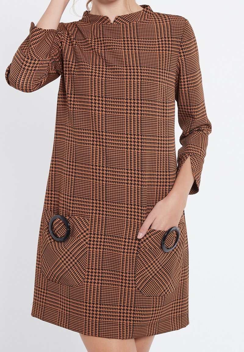 Brun och svart rutig klänning med Mandarin-krage, trekvartsärmar och två cirkulära svarta detaljer på fickorna.