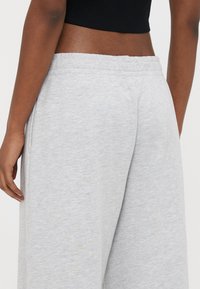 Γκρι φόρμες με μαλακή υφή, ελαστική μέση και πλαϊνές τσέπες, εμφανιζόμενες από πίσω. Χωρίς σχέδια ή εμφανείς διακοσμητικές λεπτομέρειες.