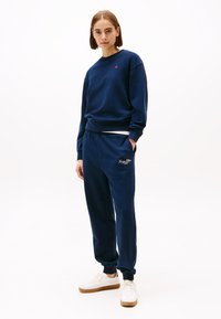 Navyblauwe sweatshirt en bijpassende joggingsbroek van zacht materiaal, met een klein logo op de borst en elastische boorden aan de broekspijpen.