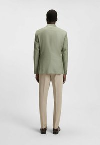 Lichtgroene op maat gemaakte jas met een gestructureerde vorm, textuurstof, enkele vent en gecombineerd met beige broeken en donkere schoenen.