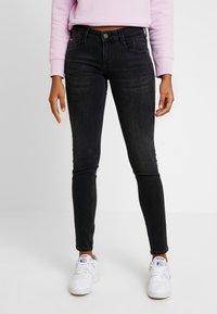 Jeans skinny negros de denim con un ligero estiramiento. Presentan un diseño clásico de cinco bolsillos y un lavado oscuro. Se combinan con zapatillas blancas.