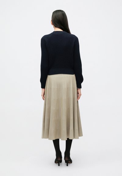 Ναυτικό μπλε ριγωτό πλεκτό πουλόβερ με κομψή κοντή γραμμή, σε συνδυασμό με μια αέρινη, πλισέ μπεζ φούστα. Μαύρες καλσόν και τακούνια ολοκληρώνουν την εμφάνιση.