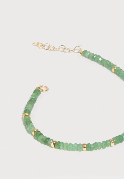 Λεπτό βραχιόλι με πράσινες λαμπερές χάντρες και μικρούς χρυσούς διαχωριστές, με χρυσή αλυσίδα προέκτασης και κούμπωμα σε ανοιχτό φόντο.