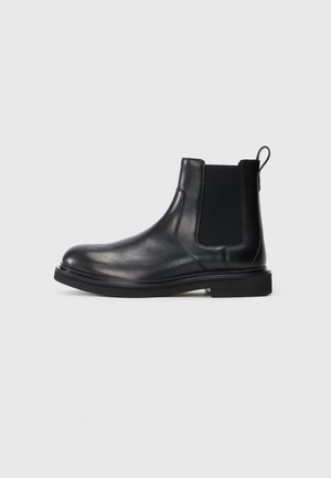 Bottines Chelsea en cuir noir avec des panneaux latéraux élastiques, bout rond et semelle plate en caoutchouc. Dispose d'une languette à l'arrière pour un enfilage facile.