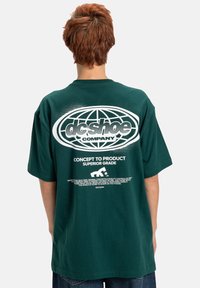 Ciemnozielona, oversize'owa koszulka z krótkim rękawem, z okrągłym dekoltem i miękkiego materiału bawełnianego, z dużym białym logo z tyłu, z napisem.