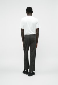 Pantaloni gri potriviți, cu două buzunare la spate, asortați cu un tricou alb simplu și teniși negri, văzuți din spate. Textură netedă.