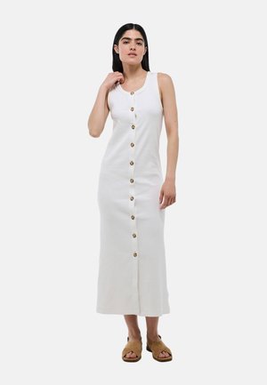 Robe maxi blanche à rayures, sans manches, présentant un devant à boutons avec de grands boutons. Le modèle porte des chaussures à enfiler marron.