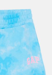 Light blue tie-dye sweatpants with an elastic waistband. Features a pink "GAP" logo on the lower right side. Soft fabric with a relaxed fit.