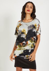 Blusa de manga corta y corte holgado en tejido ligero. Presenta un patrón abstracto multicolor con tonos en negro, blanco, naranja y verde.