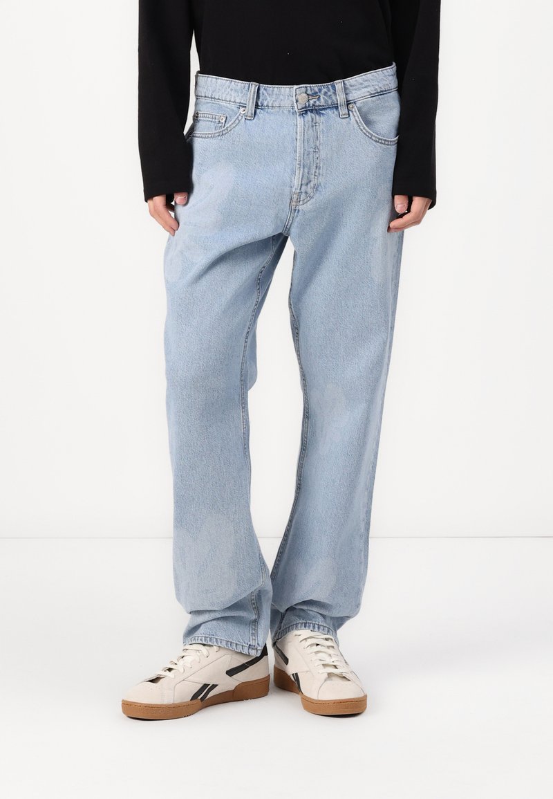 Jeans din denim de culoare albastru deschis, cu o croială lejeră, design cu cinci buzunare și o textură ușor decolorată. Asortați cu adidași de culoare albă cu accente negre.