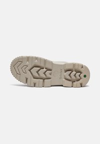 Suela de sneaker de Timberland con una textura de goma beige. El patrón de la banda de rodadura incluye surcos profundos y un acento verde cerca del talón.