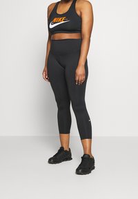 Black Nike sports bra with white and orange logo, paired with black high-waisted leggings and black athletic shoes. Smooth, fitted design.