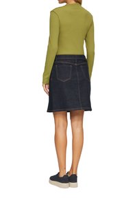 Groen langarm shirt gecombineerd met een donkere denim rok. De rok heeft twee achterzakken en oranje stiksels. Zwarte schoenen met een getextureerde zool.