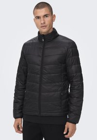Svart puffjakke med quiltet design, høy krage, frontglidelås og to sidelommer. Glatt, lett stoff med subtil glans.